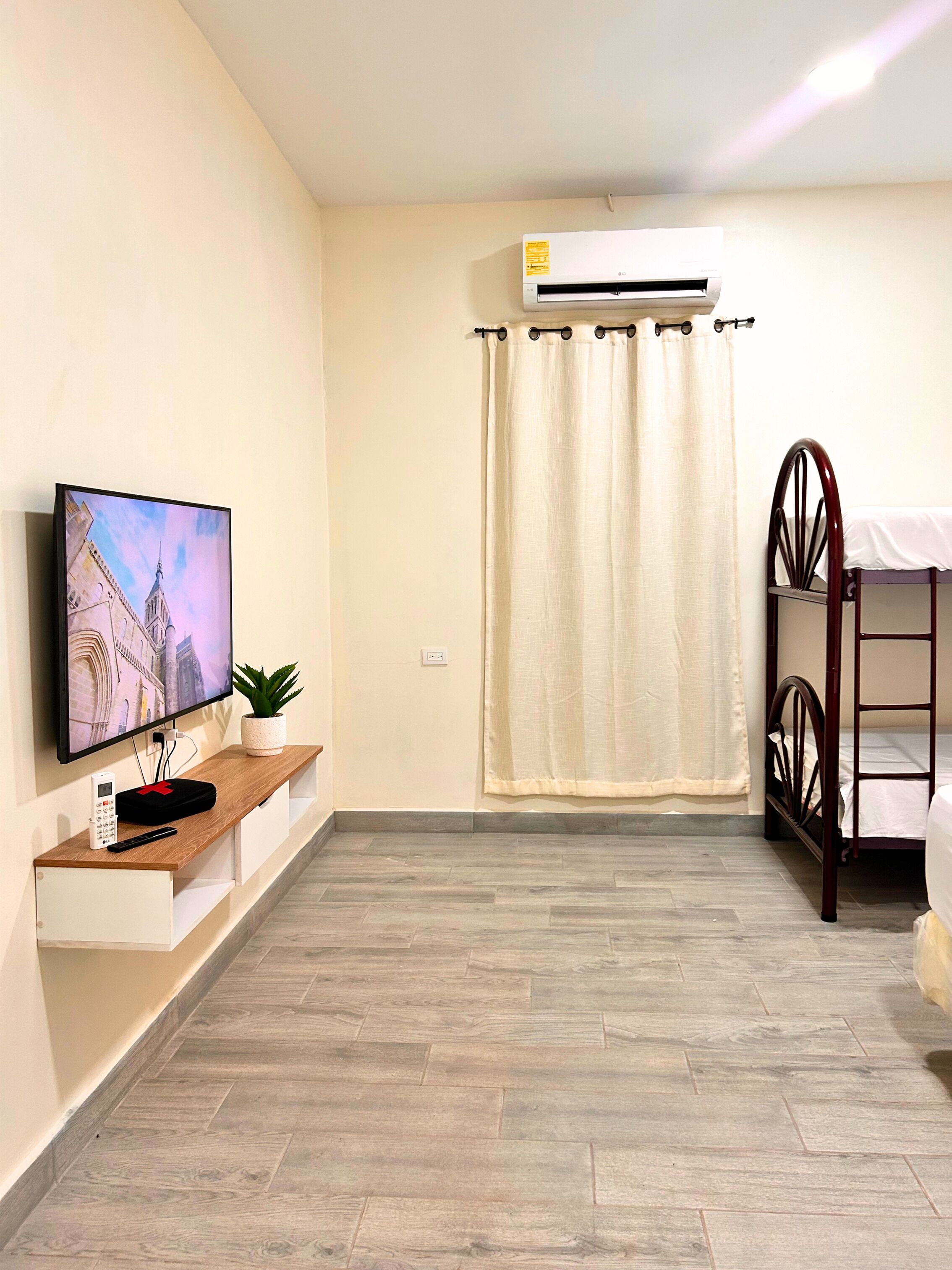 Ein Zimmer mit Fernseher, einer kleinen Pflanze, einem Etagenbett und einer Klimaanlage.