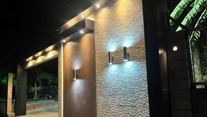 Facciata moderna di un edificio con parete in pietra strutturata, pannello verticale in legno e due luci a parete.