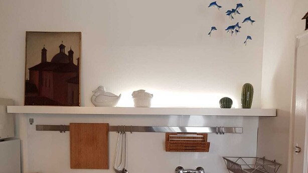 A kitchen with a stainless steel sink, white cabinets, a wooden shelf with decorative items, and a wall-mounted rack. - Panoramic view in San Marco overlooking the rooftops (Venezia)
