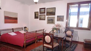 A room with a bed, a table with chairs, a rug, and several framed pictures on the wall. - Panoramic view in San Marco overlooking the rooftops (Venezia)
