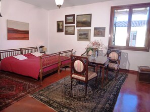 Ein Zimmer mit einem Bett, einem Tisch mit Stühlen, einem Teppich und mehreren gerahmten Bildern an der Wand.