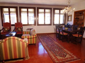 Ein geräumiges Wohnzimmer mit großem Teppich, gestreiften Sofas, einem Esstisch mit Stühlen und einer Pendelleuchte.