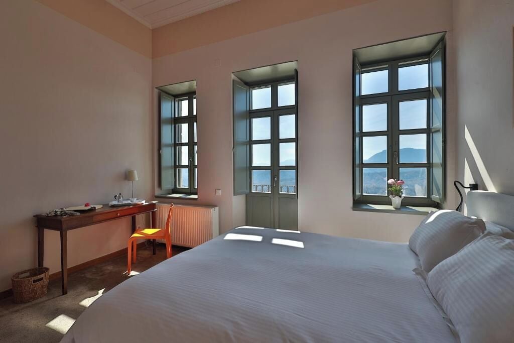 Habitación de hotel con cama, escritorio, silla y tres ventanas amplias con vistas.