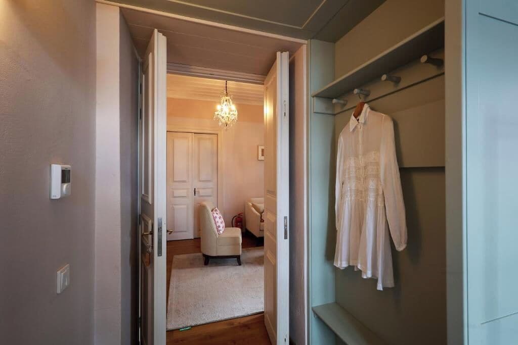 Un espacio interior con una puerta blanca que da a una habitación con una silla blanca y una araña.