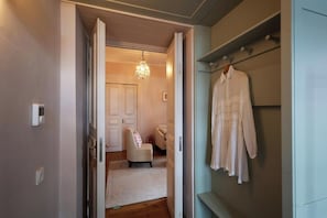 An interior space with a white door leading to a room with a white chair and a chandelier.