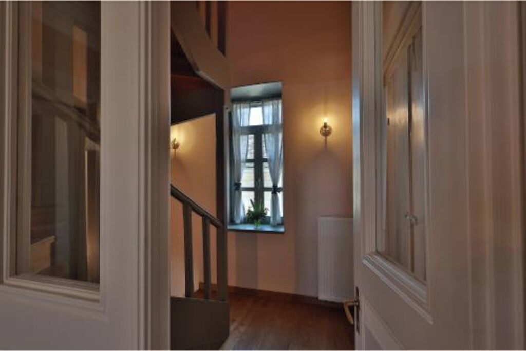 A hallway with a staircase, a window with curtains, and wall-mounted lighting.