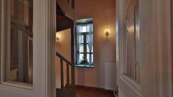 A hallway with a staircase, a window with curtains, and wall-mounted lighting.