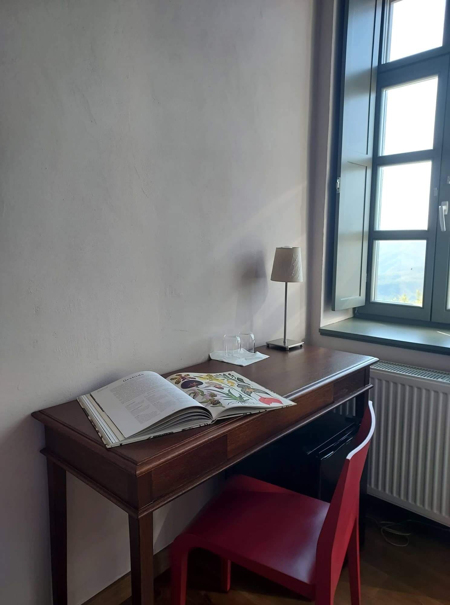A room with a wooden desk, a red chair, a window with a view, and a radiator.