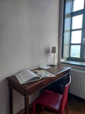 A room with a wooden desk, a red chair, a window with a view, and a radiator.