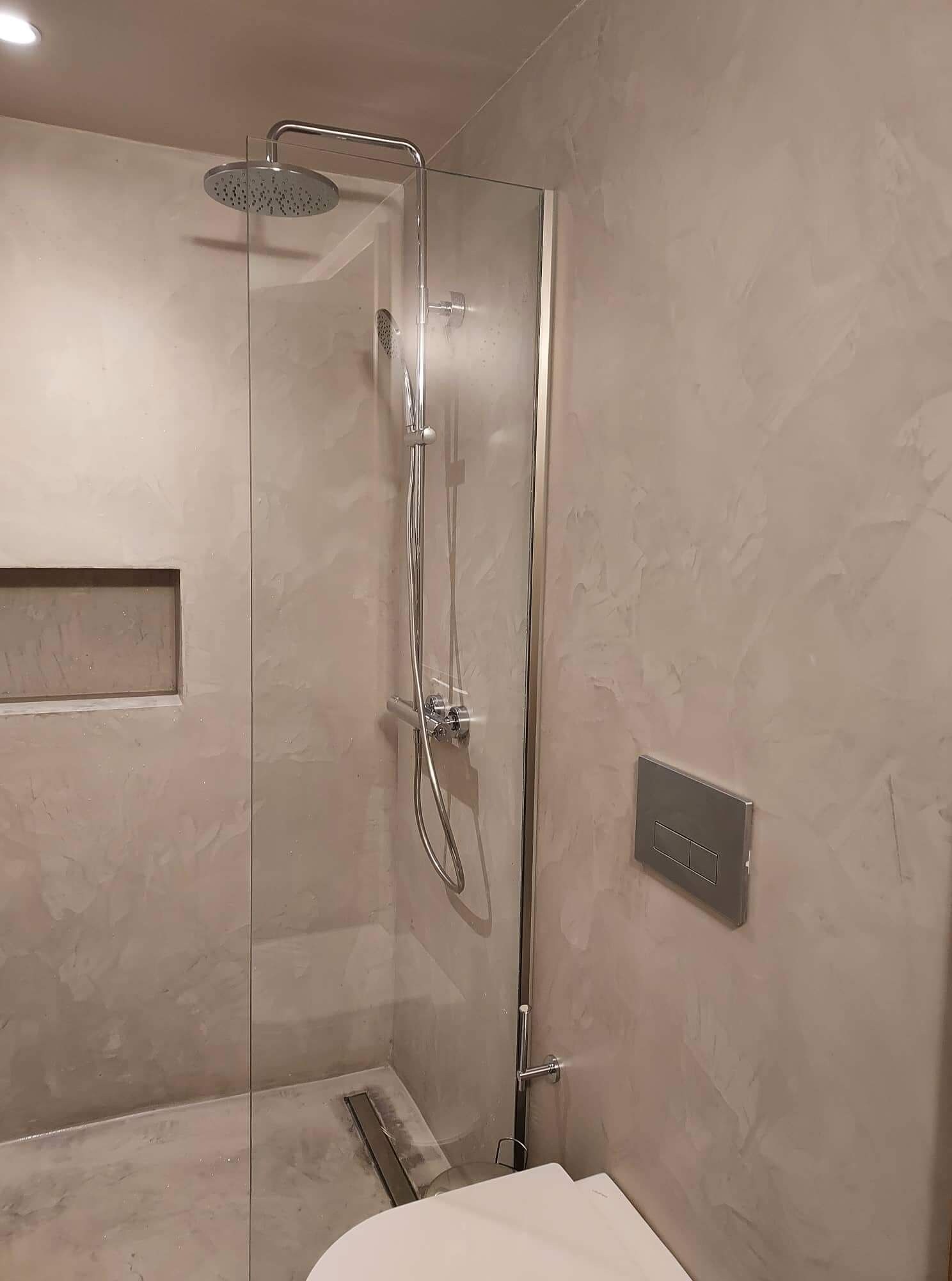 Een moderne badkamer met een douchecabine van glas, een handdouche en een bedieningspaneel aan de muur.
