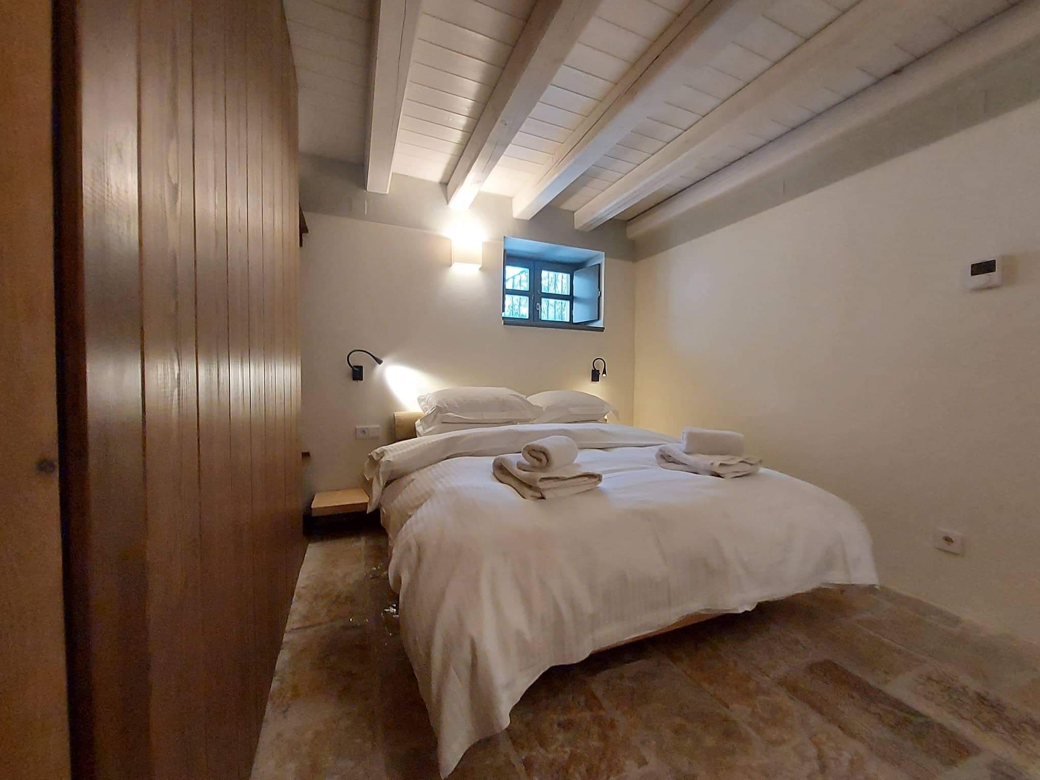 Un dormitorio con cama, mesita de noche, ventana y lámpara de pared.