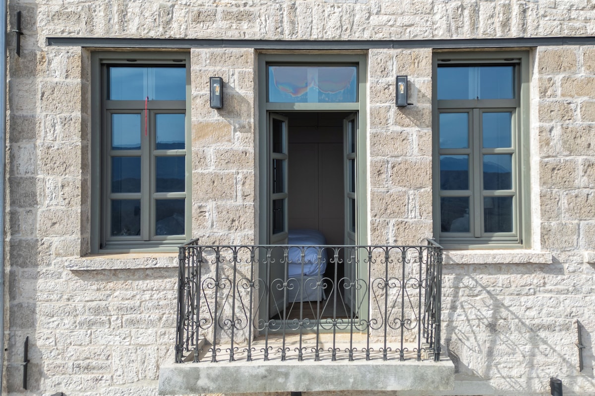Un bâtiment en pierre doté de trois fenêtres, d’un balcon avec une balustrade en fer forgé et d’une porte donnant sur une pièce.