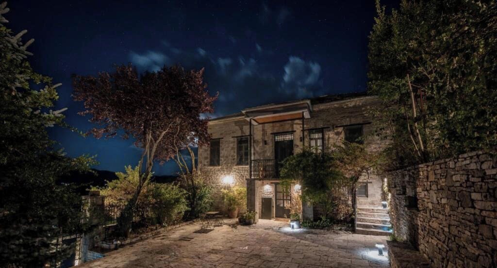 A stone building with a staircase leading to the entrance, surrounded by trees and a clear night sky.