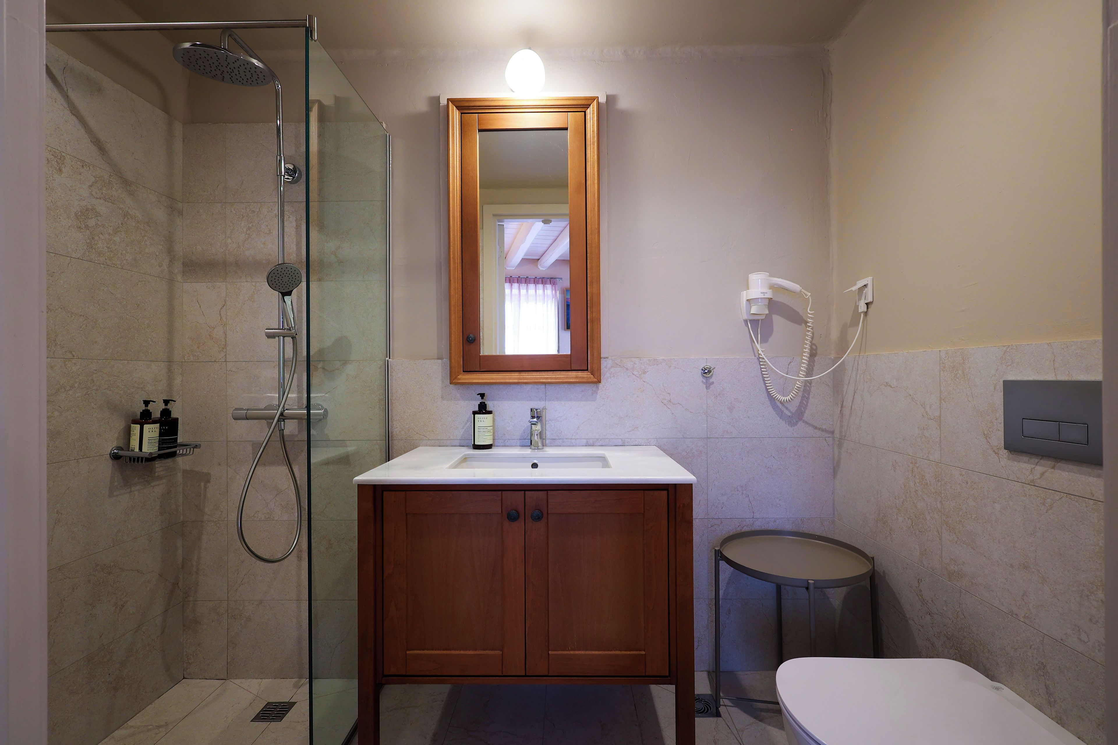 Un baño con ducha de vidrio, tocador de madera con espejo y un inodoro.