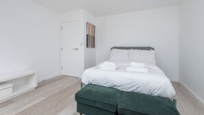 A minimalist bedroom with a bed, a bench, and a door. - Bright Modern 3BDR Family Home with Private Patio (Greater London)