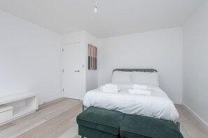 Ein schlicht eingerichtetes Schlafzimmer mit Bett, Bank und Tür.