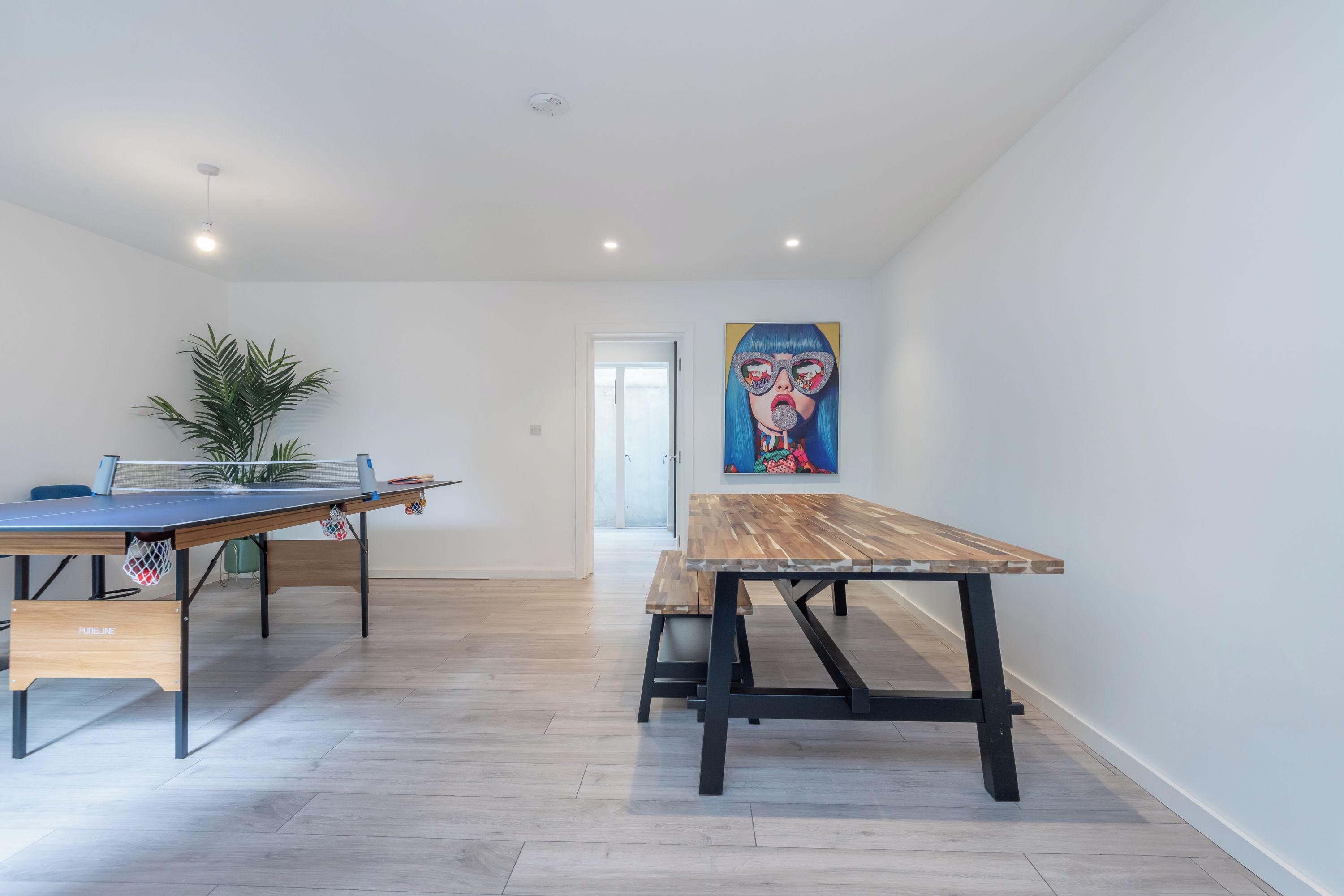 Un espace repas moderne avec une table de ping-pong, une table en bois et un tableau accroché au mur.