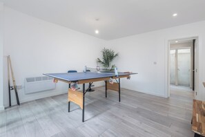 Ein Zimmer mit einem Tischtennis-Tisch, einer Topfpflanze und einer Tür zu einem weiteren Raum.