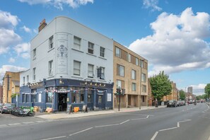 A pub named 'The Grosvenor Arms' with a traditional facade, multiple windows, and a sign indicating it offers food and a room for hire. - Bright Modern 3BDR Family Home with Private Patio (Greater London)