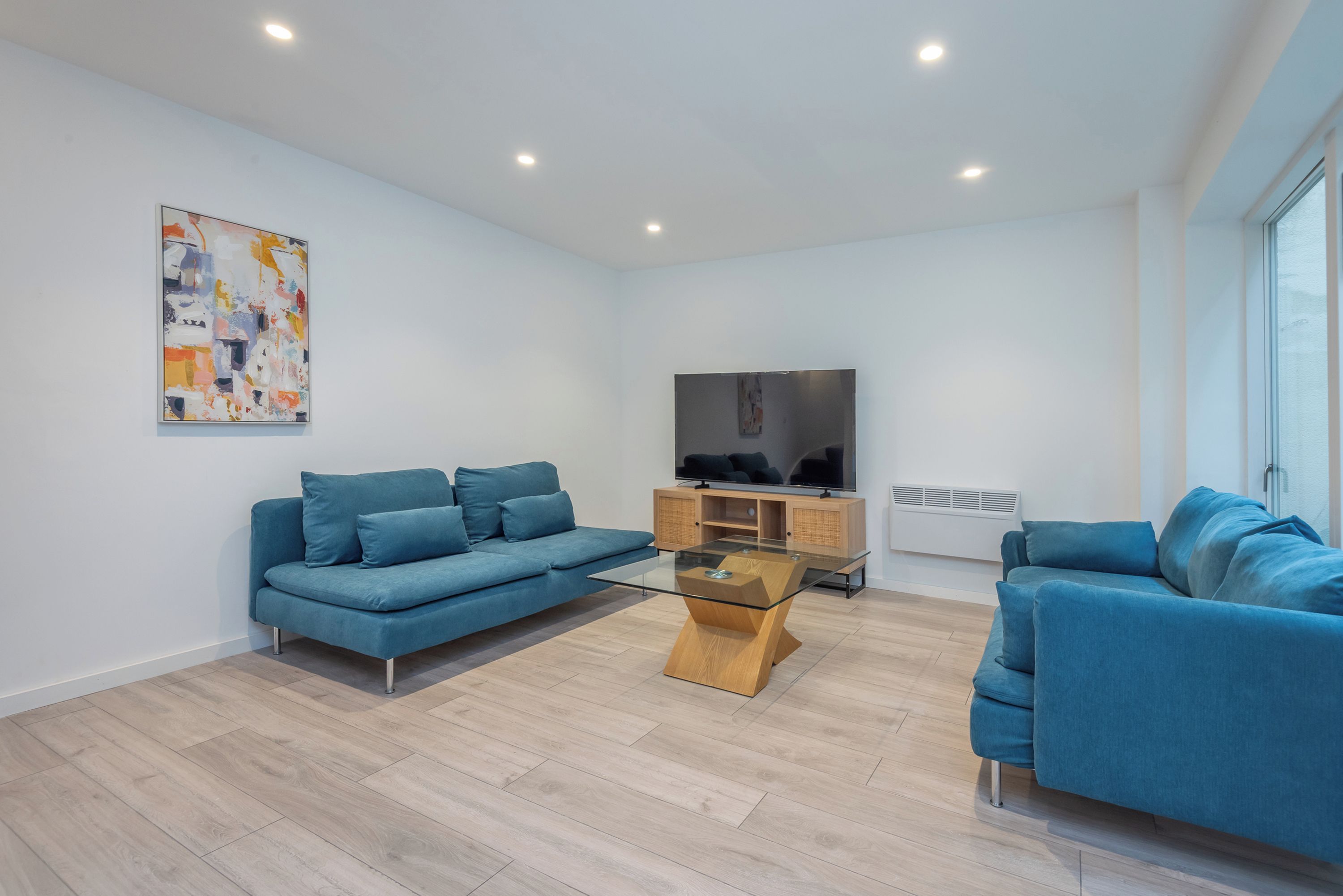 Un salon moderne avec un canapé bleu, une table basse en verre et un téléviseur posé sur un meuble en bois.