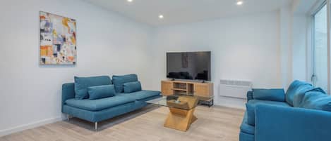 Una sala moderna con un sofá azul, una mesa de centro de vidrio y un televisor sobre un mueble de madera.