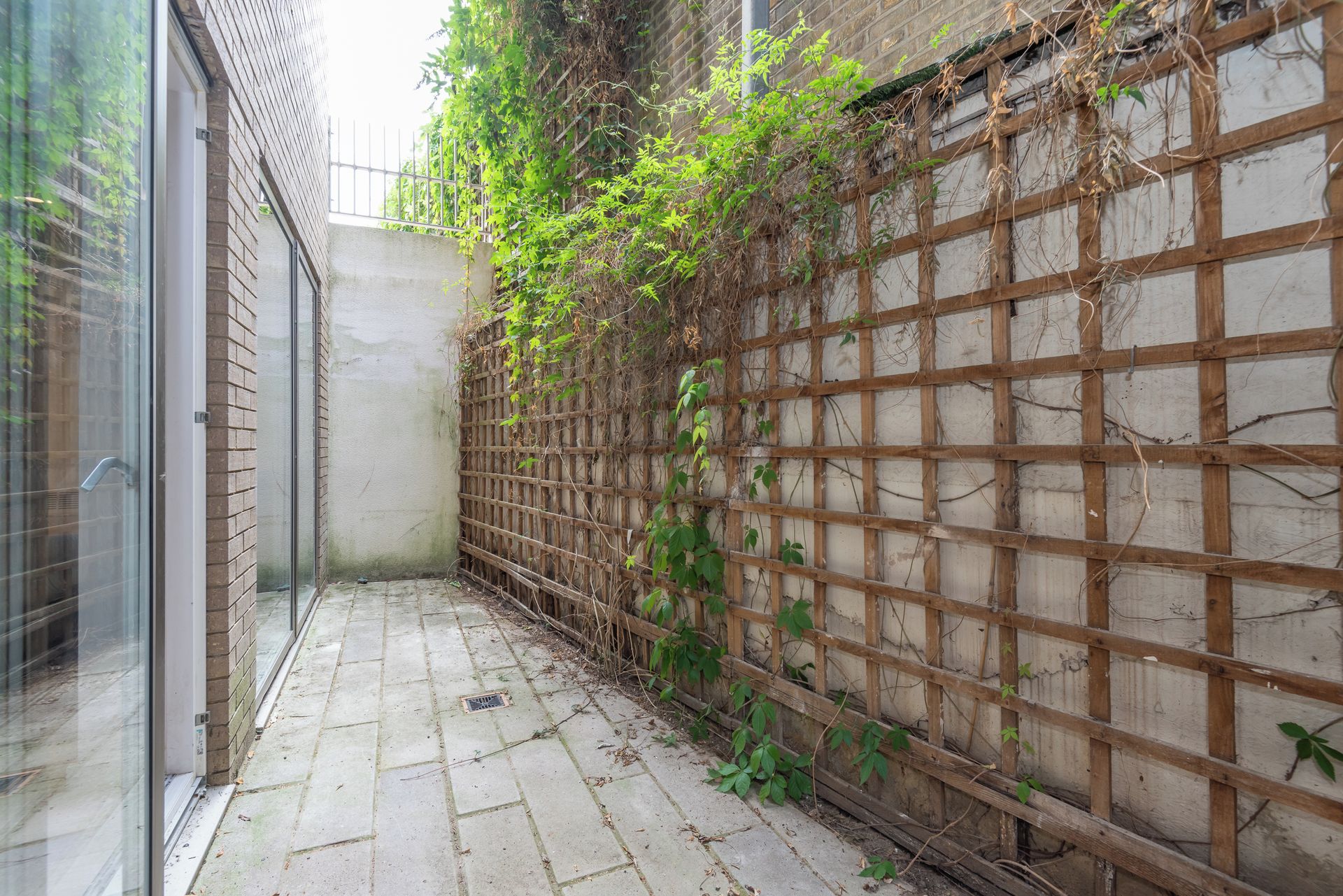 A narrow alleyway with a wooden lattice fence, a concrete wall, and a tiled floor.