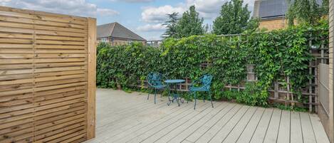 A wooden deck with a metal fence, two blue metal chairs, and a table.