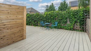 A wooden deck with a metal fence, two blue metal chairs, and a table. - Bright Modern 3BDR Family Home with Private Patio (Greater London)