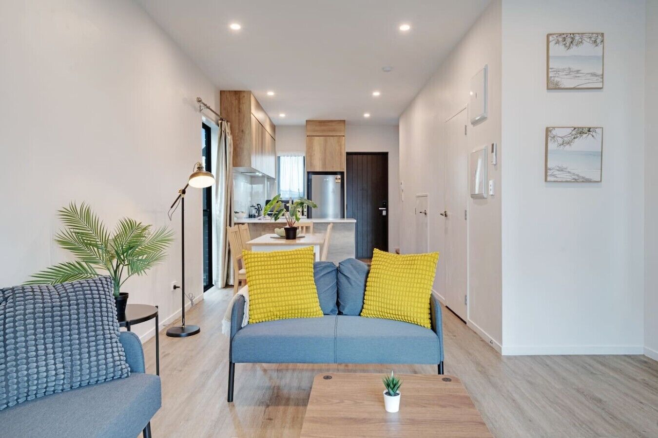 A modern living room with a sofa, a coffee table, and a dining area in the background.