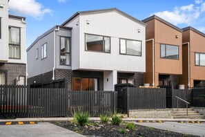 A modern residential building with a flat roof, large windows, and a black fence.