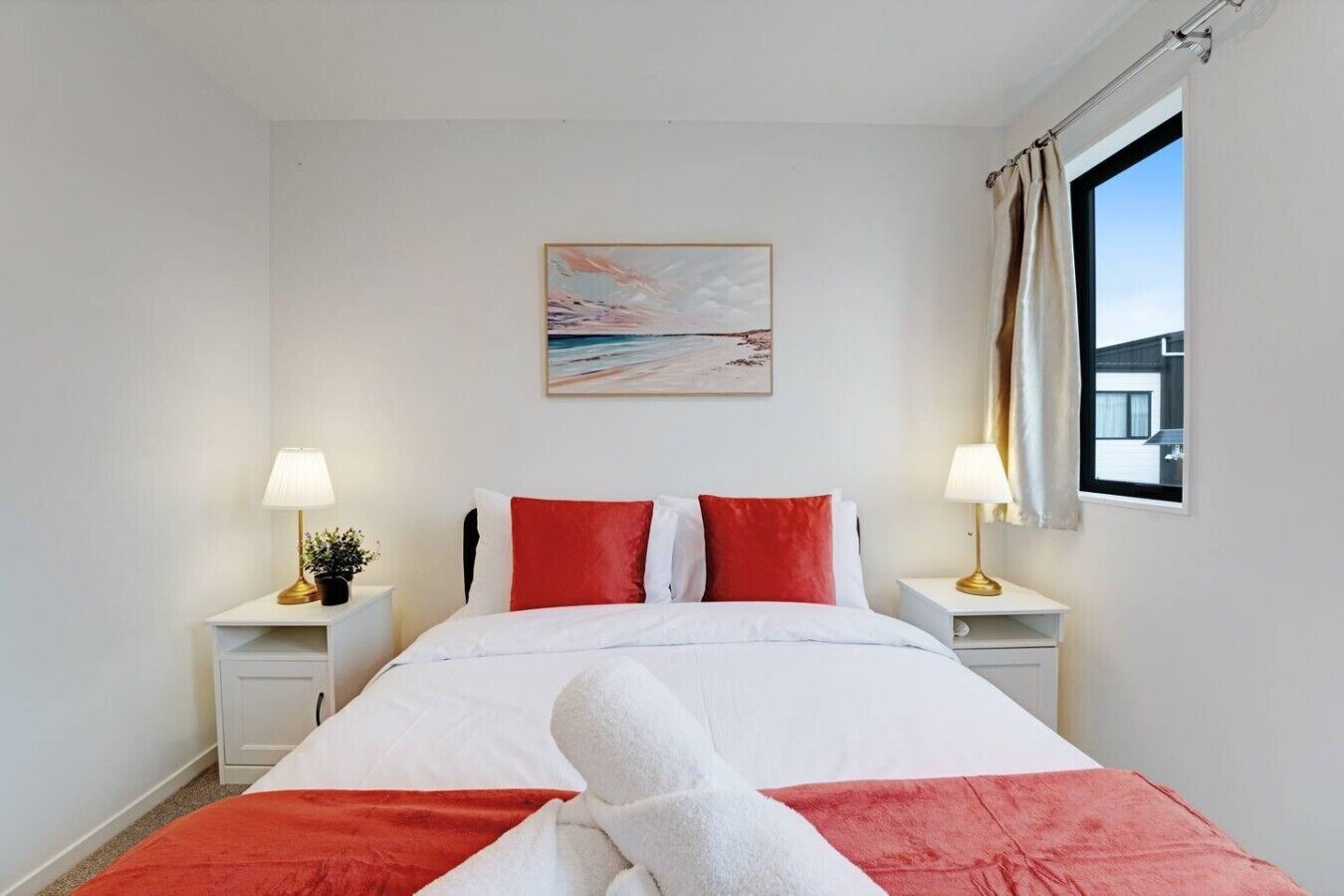 Una camera d'hotel con un letto, due comodini con lampade, una finestra con tende e un quadro appeso al muro.