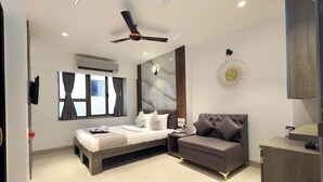 A modern bedroom with a bed, a sofa, a ceiling fan, and a decorative wall piece. - Myotel - Andheri (Mumbai)