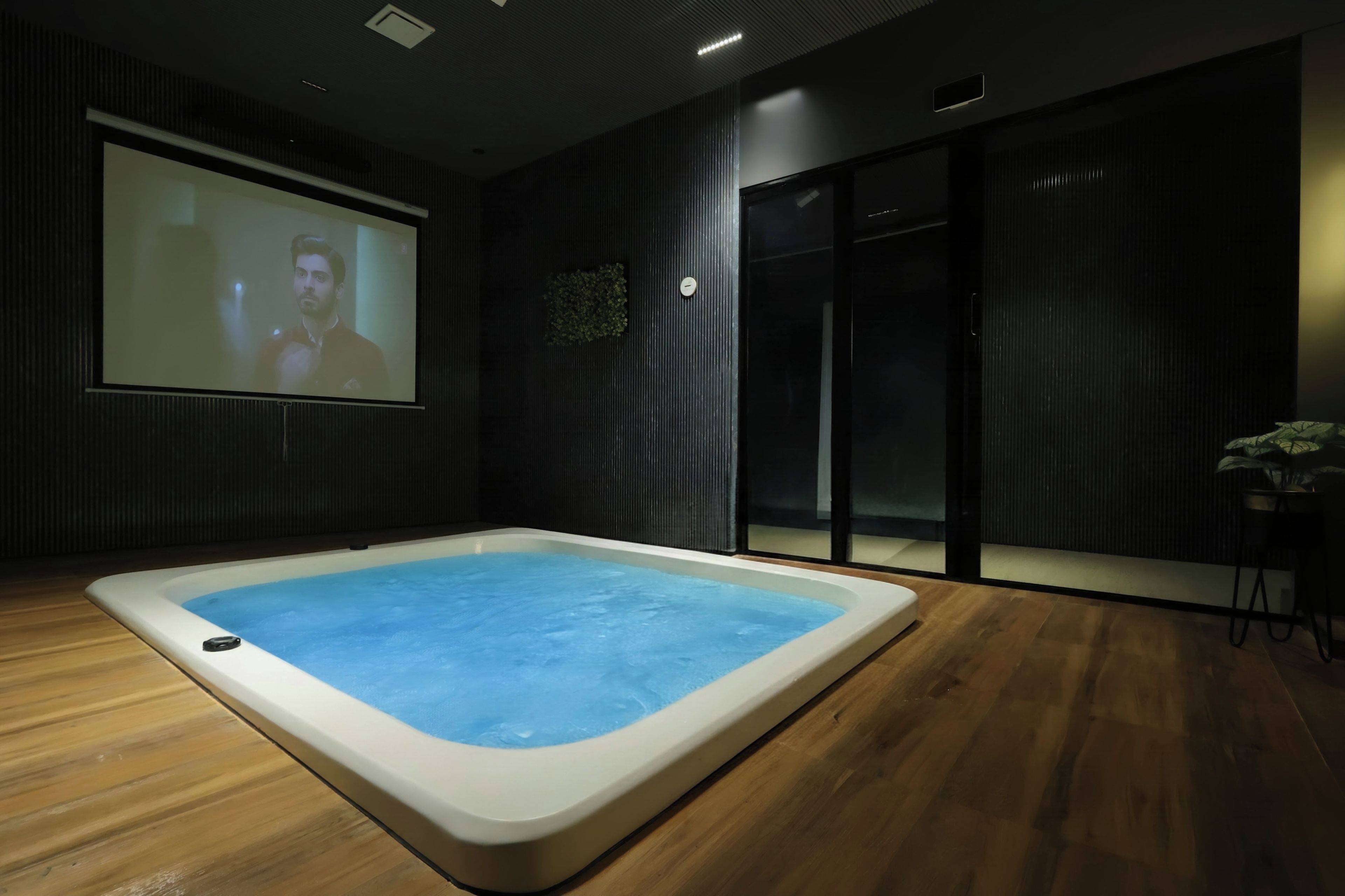 A modern room with a large screen displaying a person, a hot tub, and a sliding door.