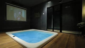 A modern room with a large screen displaying a person, a hot tub, and a sliding door.