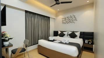A modern hotel room with a bed, a ceiling fan, a wall-mounted abstract art piece, and a small table with a vase of flowers.