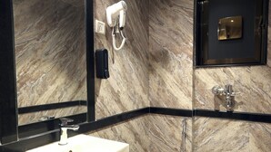 Un baño moderno con pared de mármol, un espejo grande, un lavamanos, un inodoro y zona de ducha.