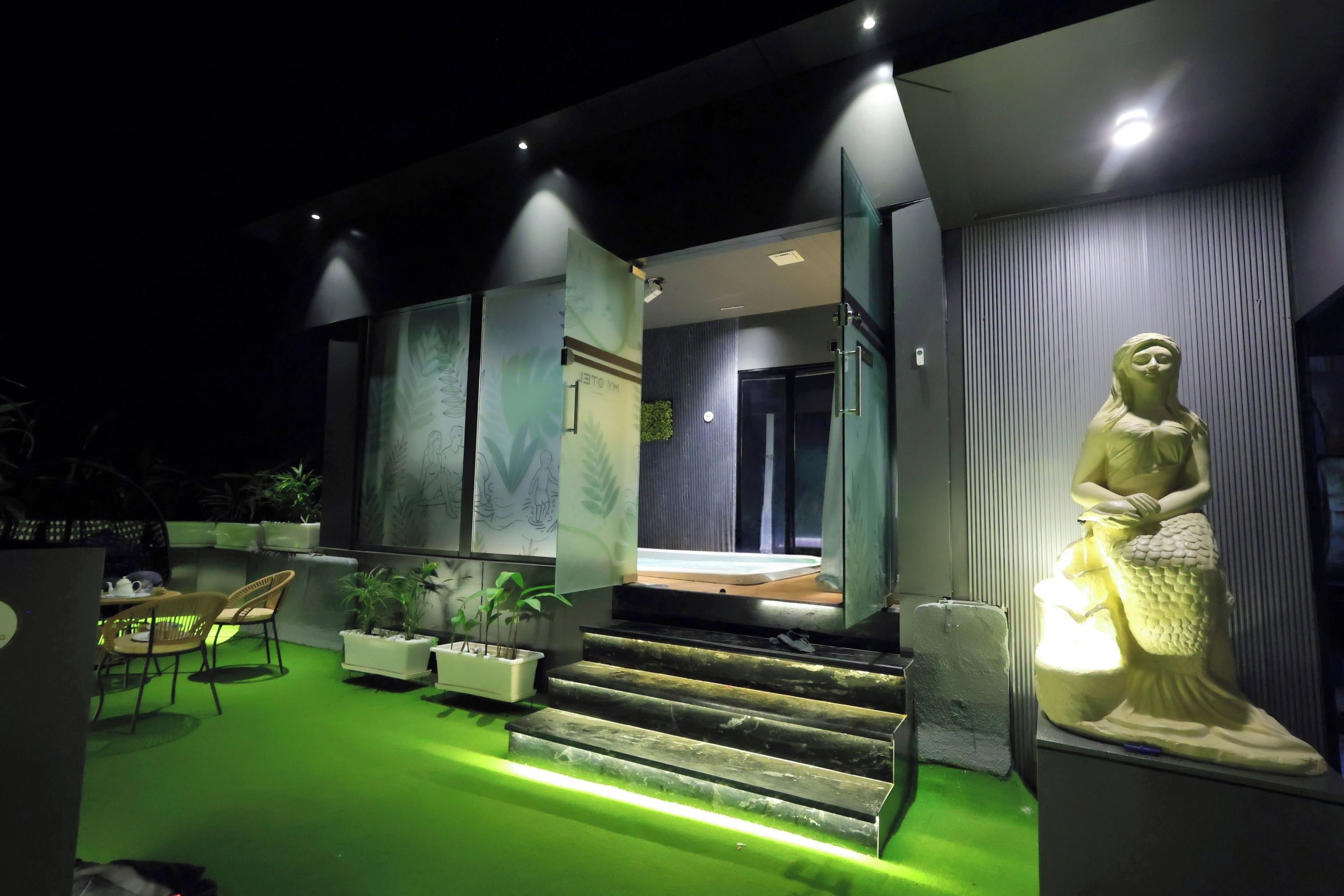 A modern building with a green-lit entrance, a statue, and outdoor seating.