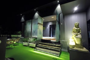 Edifici modern amb entrada il·luminada de verd, una estàtua i seients a l'exterior.