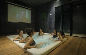 Un grupo de personas en una piscina cubierta climatizada con una pantalla grande mostrando una película.