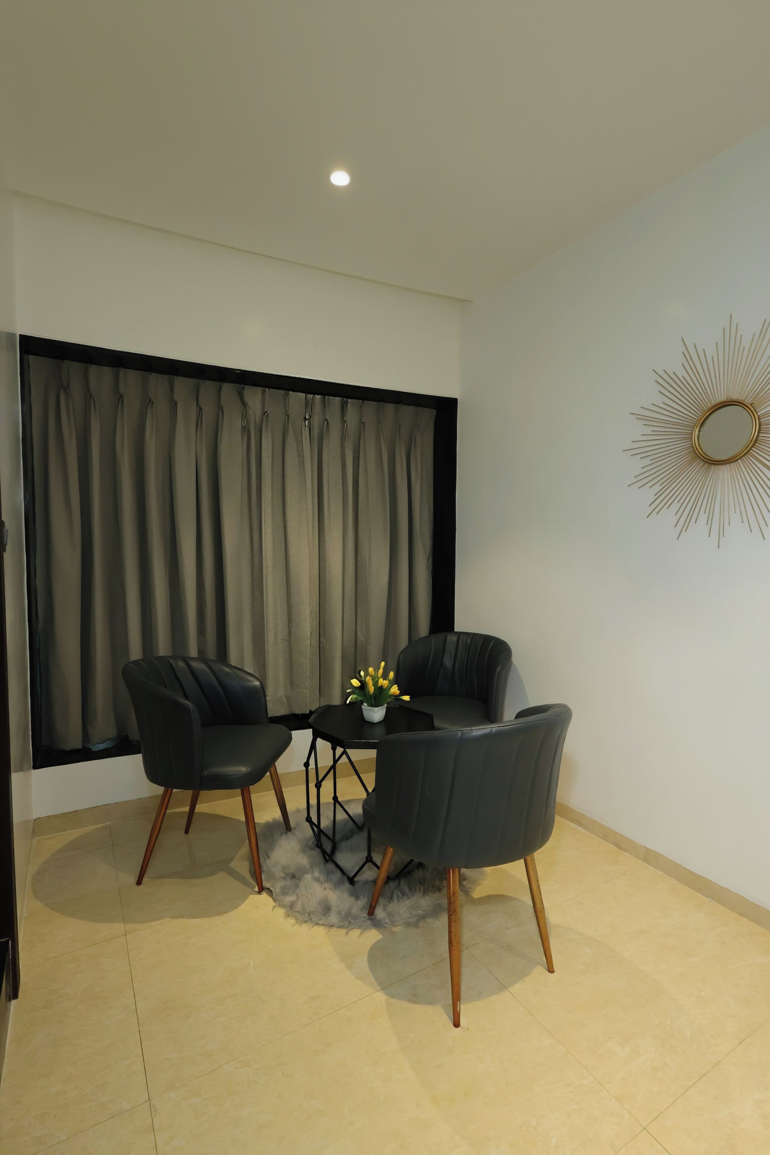 A modern room with two black chairs, a small table, a potted plant, and a decorative mirror on the wall.