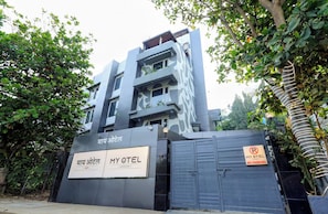 Un hotel moderno con entrada protegida, un letrero con el nombre del hotel y un letrero de 'prohibido estacionar'.