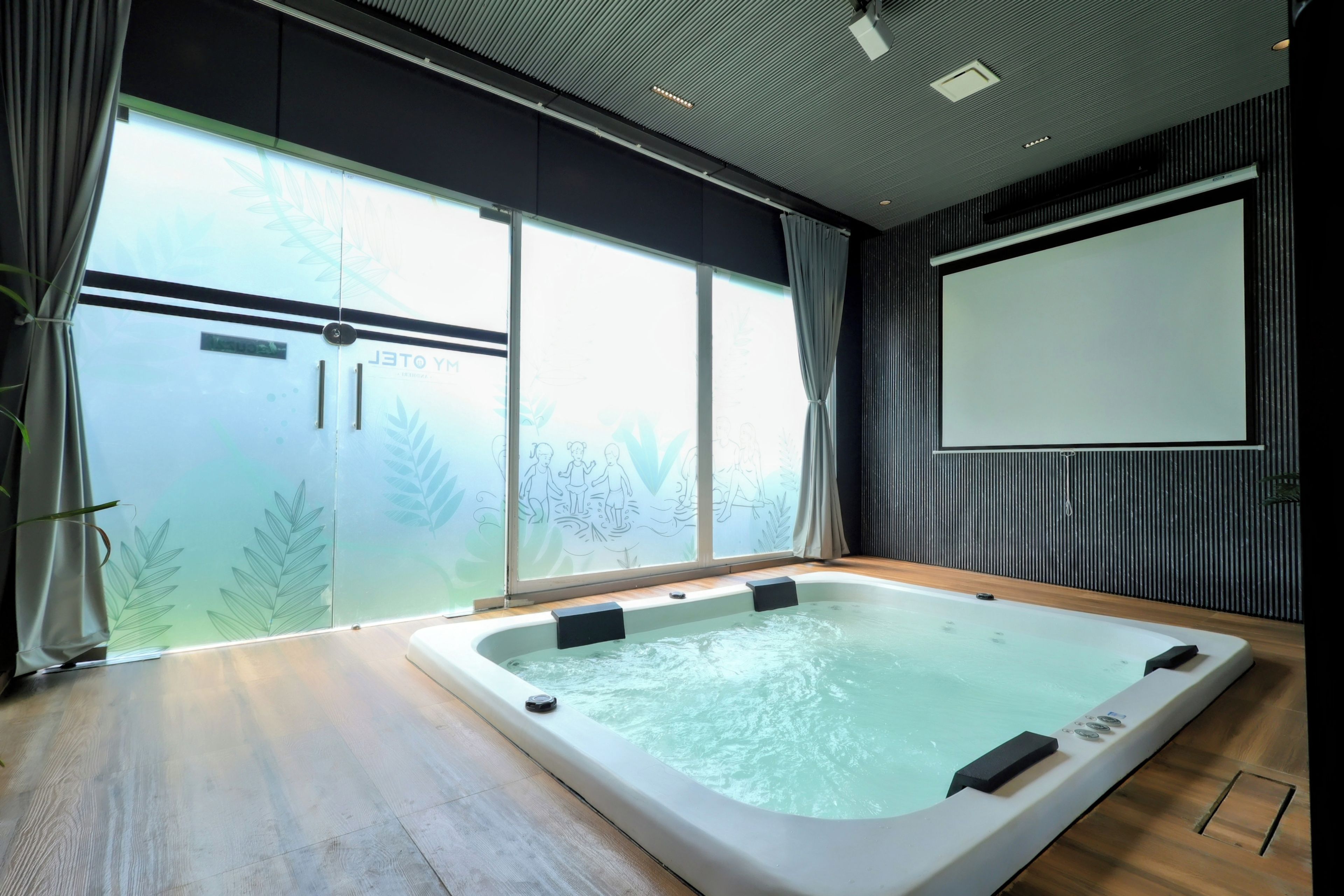 Un moderno spa con un amplio hidromasaje, una puerta corrediza de vidrio que da a un jardín y una pantalla de proyector en la pared.