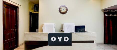 A reception desk with a sign reading 'OYO,' a clock on the wall, and a ceiling fan.