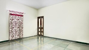 A room with a tiled floor, a door with a window, and a curtain with a floral pattern. - The Baba Guest House (Indore)
