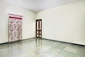 A room with a tiled floor, a door with a window, and a curtain with a floral pattern. - The Baba Guest House (Indore)