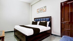 A bedroom with a wooden bed, white bedding, a blue headboard, and a wooden door. - The Baba Guest House (Indore)