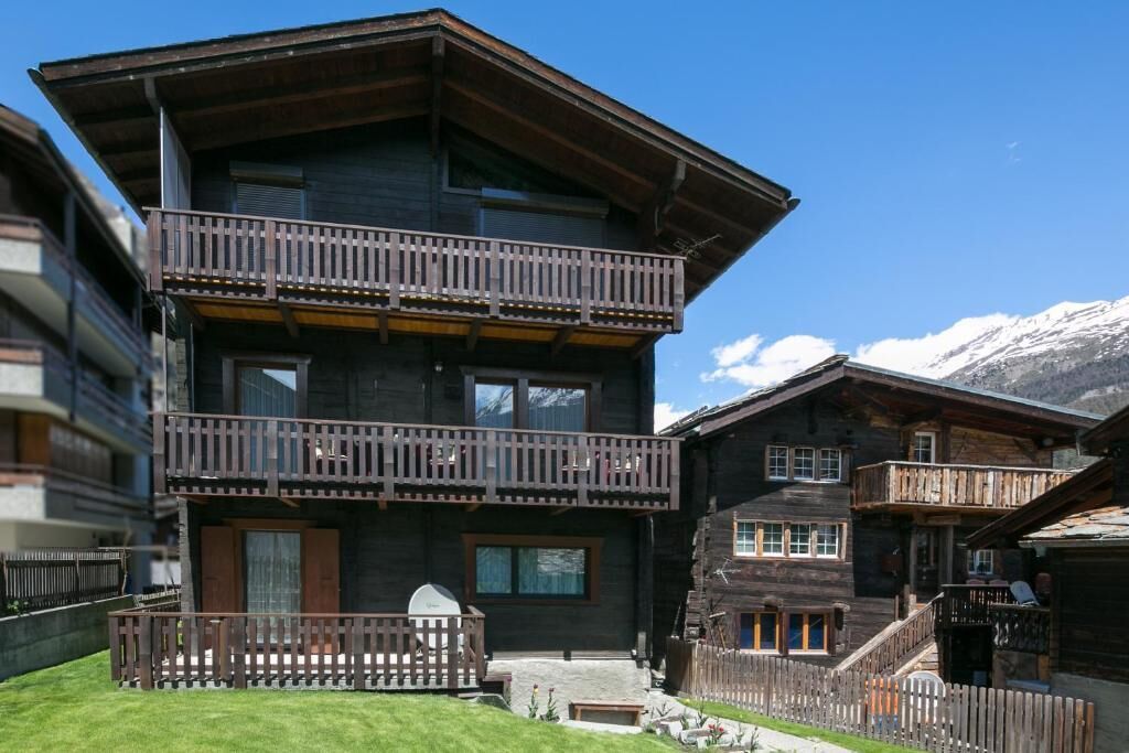 Un edificio de madera de varios pisos con balcones, un sendero de piedra y montañas al fondo.