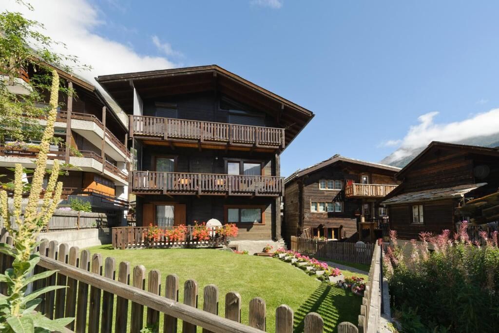 Ein mehrstöckiges Holzchalet mit Balkonen, einem gepflegten Rasen und einem Holzzaun.