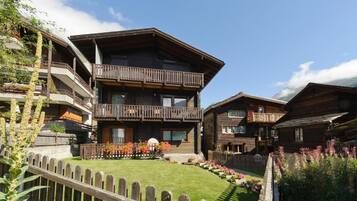 Ein mehrstöckiges Holzchalet mit Balkonen, einem gepflegten Rasen und einem Holzzaun.