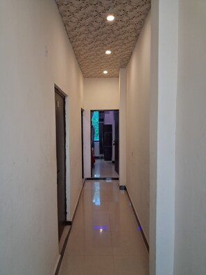 A corridor with a patterned ceiling, a door on the left, and a hallway leading to a room with a purple wall. - Ladli homes  (Mathura)